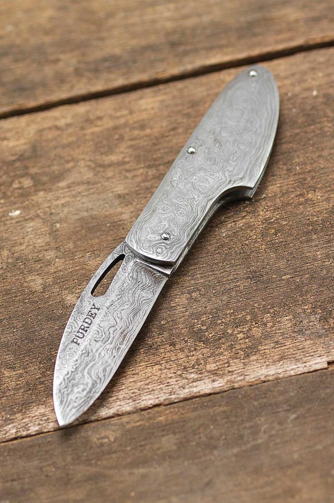 A very useful folding pocket knife made from Damascus steel. The sidelock-shaped knife features traditional gun scroll engraving.